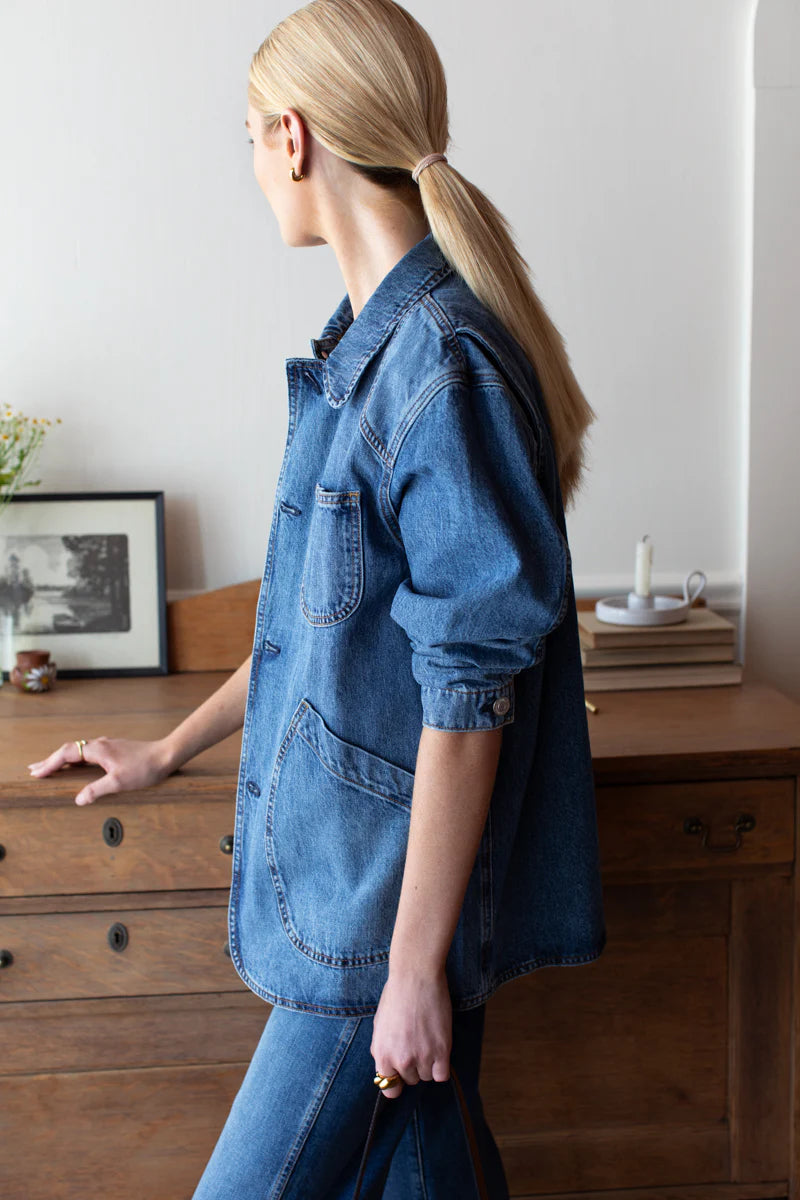 Person wearing a denim shirt standing in front of a wooden dresser.