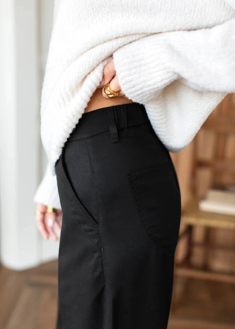 Person wearing a white sweater and black pants with a blurred background