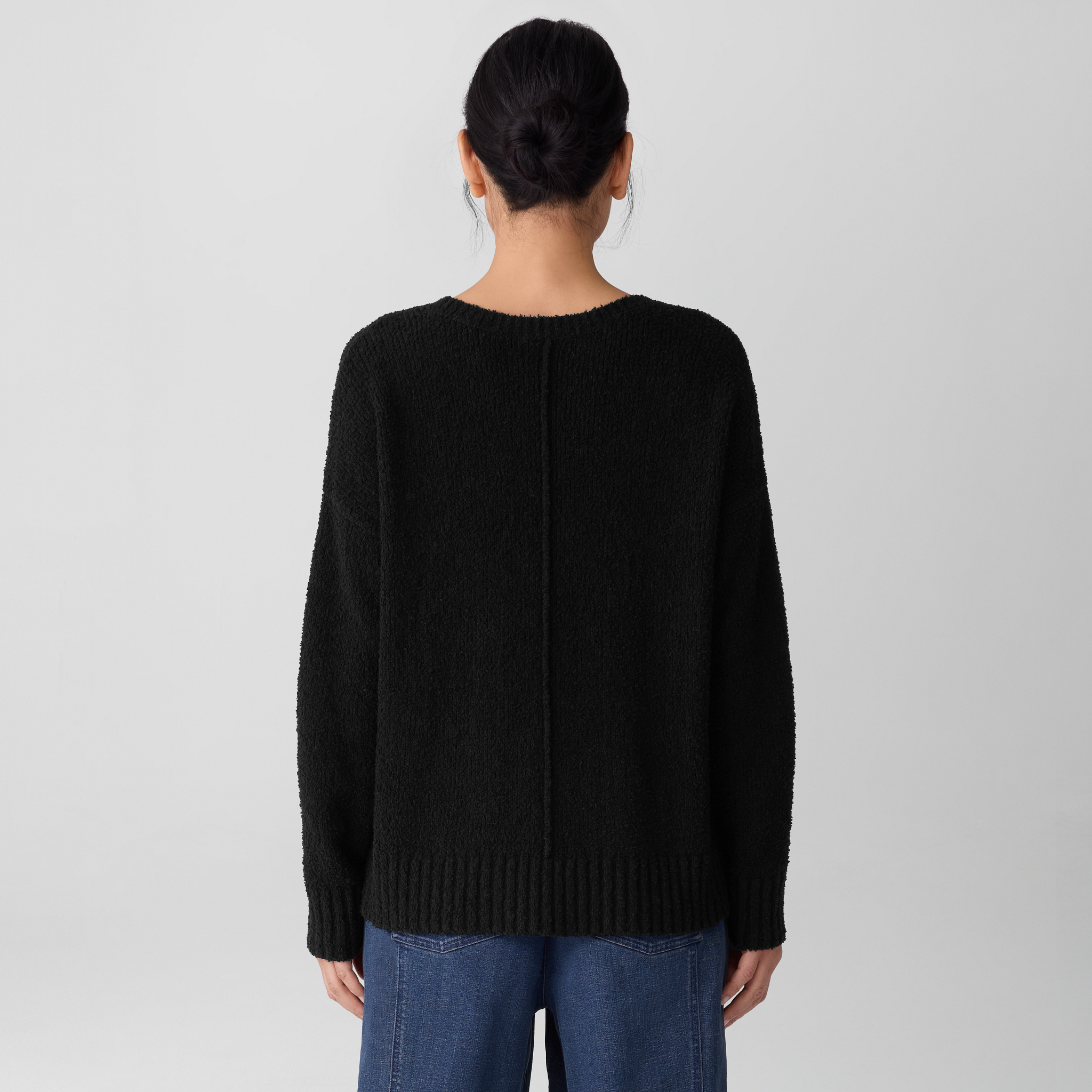 Back of woman wearing an Eileen Fisher crewneck sweater in Woodland and blue jeans on a plain background