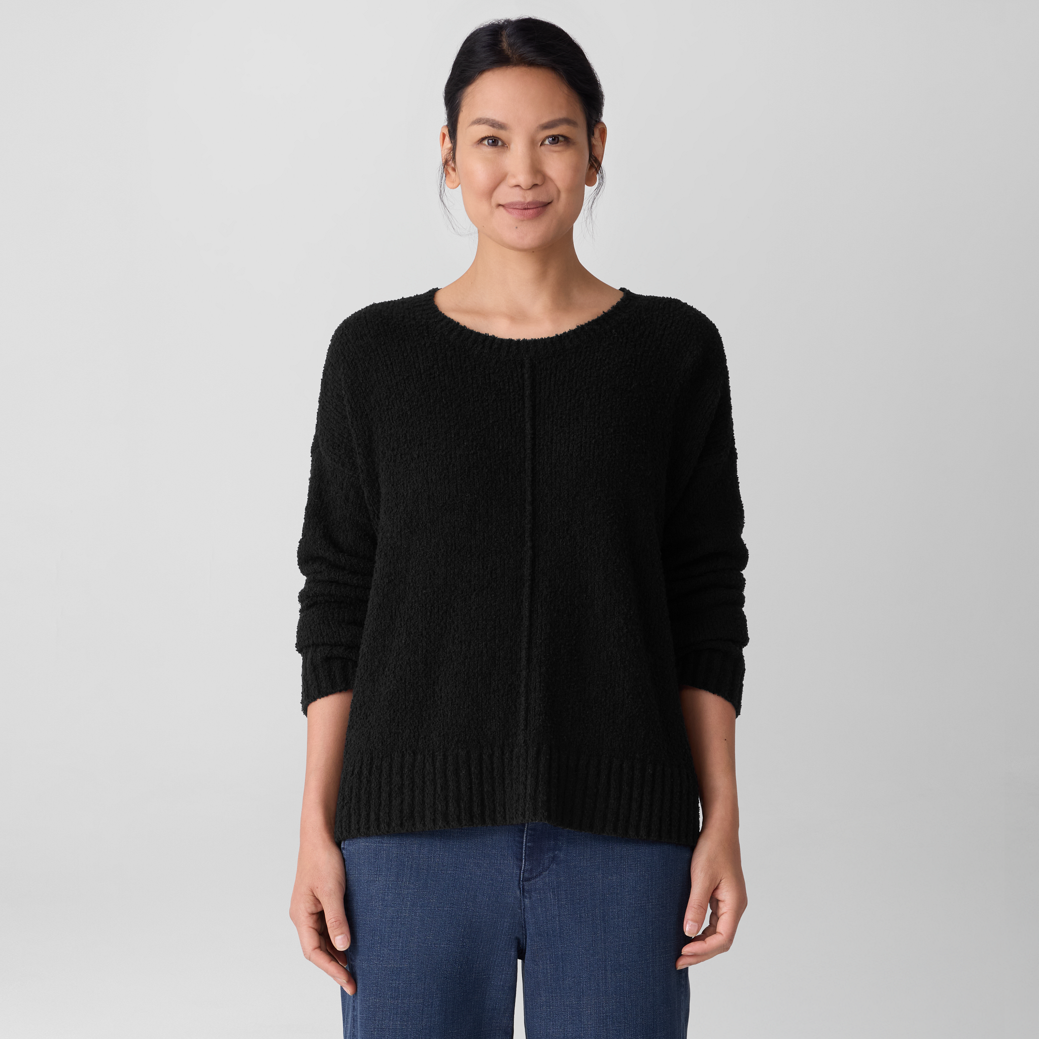 Woman wearing an Eileen Fisher Crewneck sweater in Woodland and blue jeans on a plain background