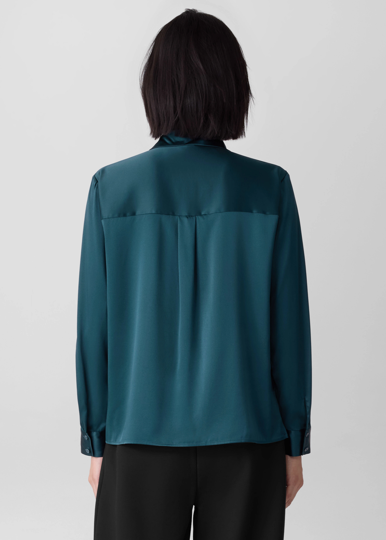 Women wearing an Eileen Fisher teal shirt in the color Alpine on a plain background