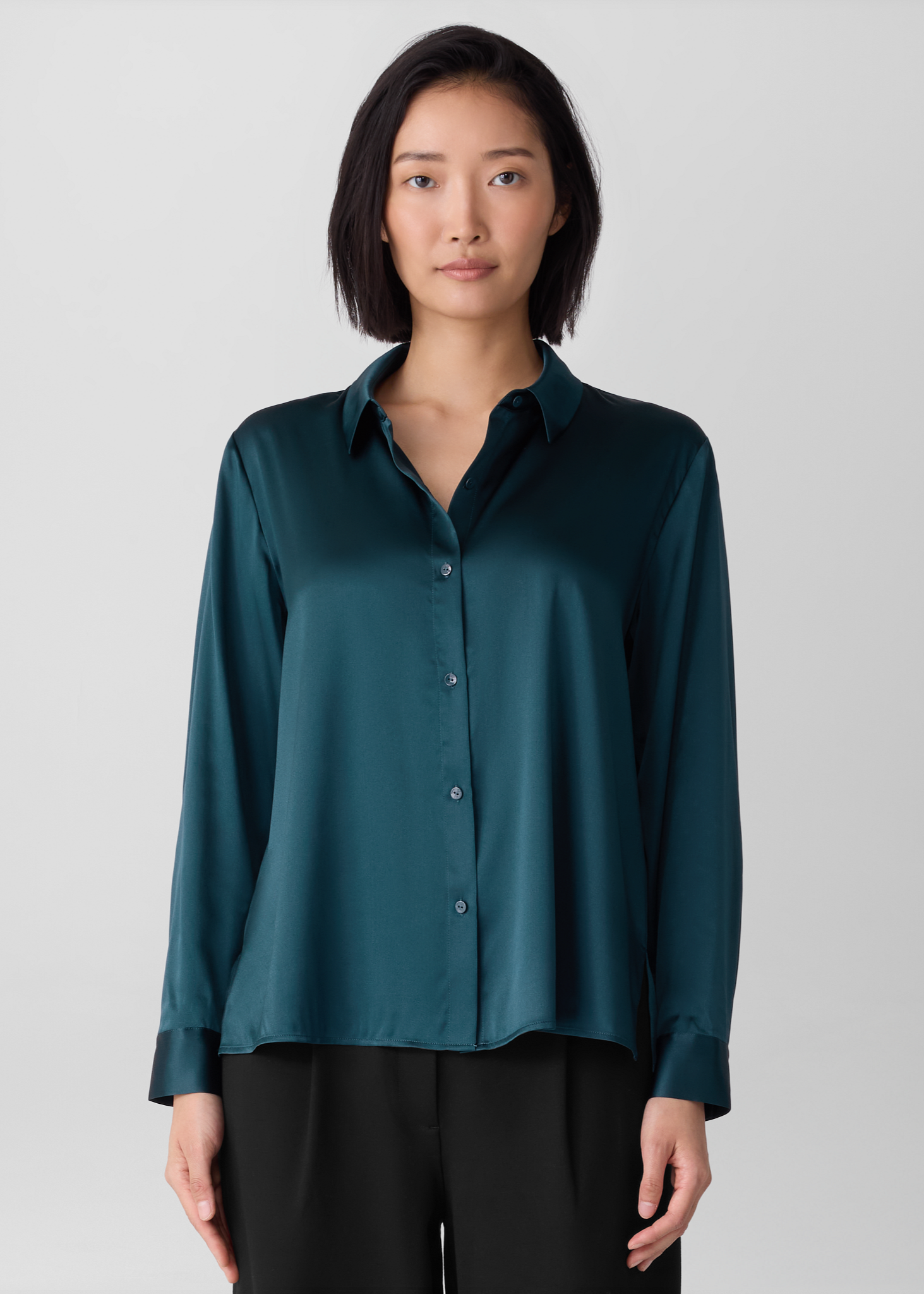 Woman wearing an Eileen Fisher teal shirt in the color Alpine against a gray background