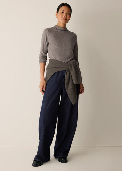 A woman modeling a gray mock-neck knit sweater with a tied waist detail, paired with dark wide-leg trousers, against a plain light beige studio background.