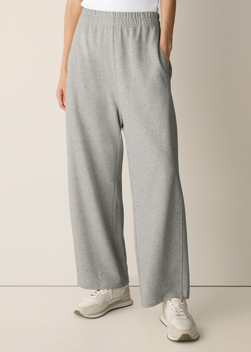 A person wearing light heather gray wide-leg sweatpants with an elastic waistband and side pockets, paired with white sneakers against a plain beige studio background.