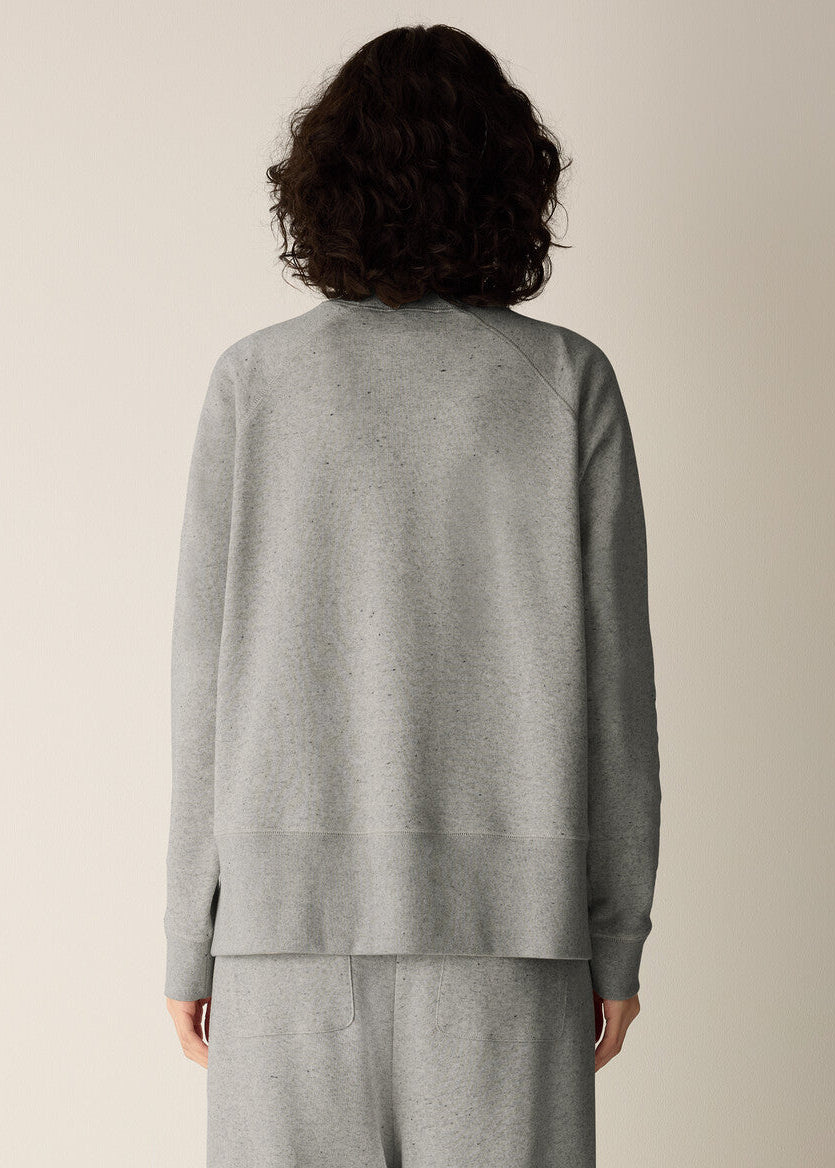 A person shown from the back wearing a light gray knit top and matching gray bottoms against a plain warm beige studio background.