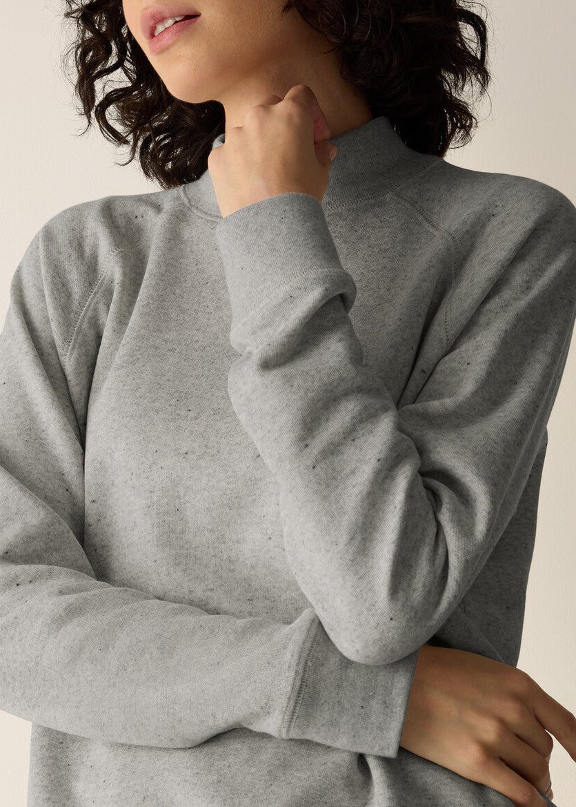 A close-up of a person wearing a light gray heather crewneck sweatshirt, showing the texture of the fabric and the mock neck design.