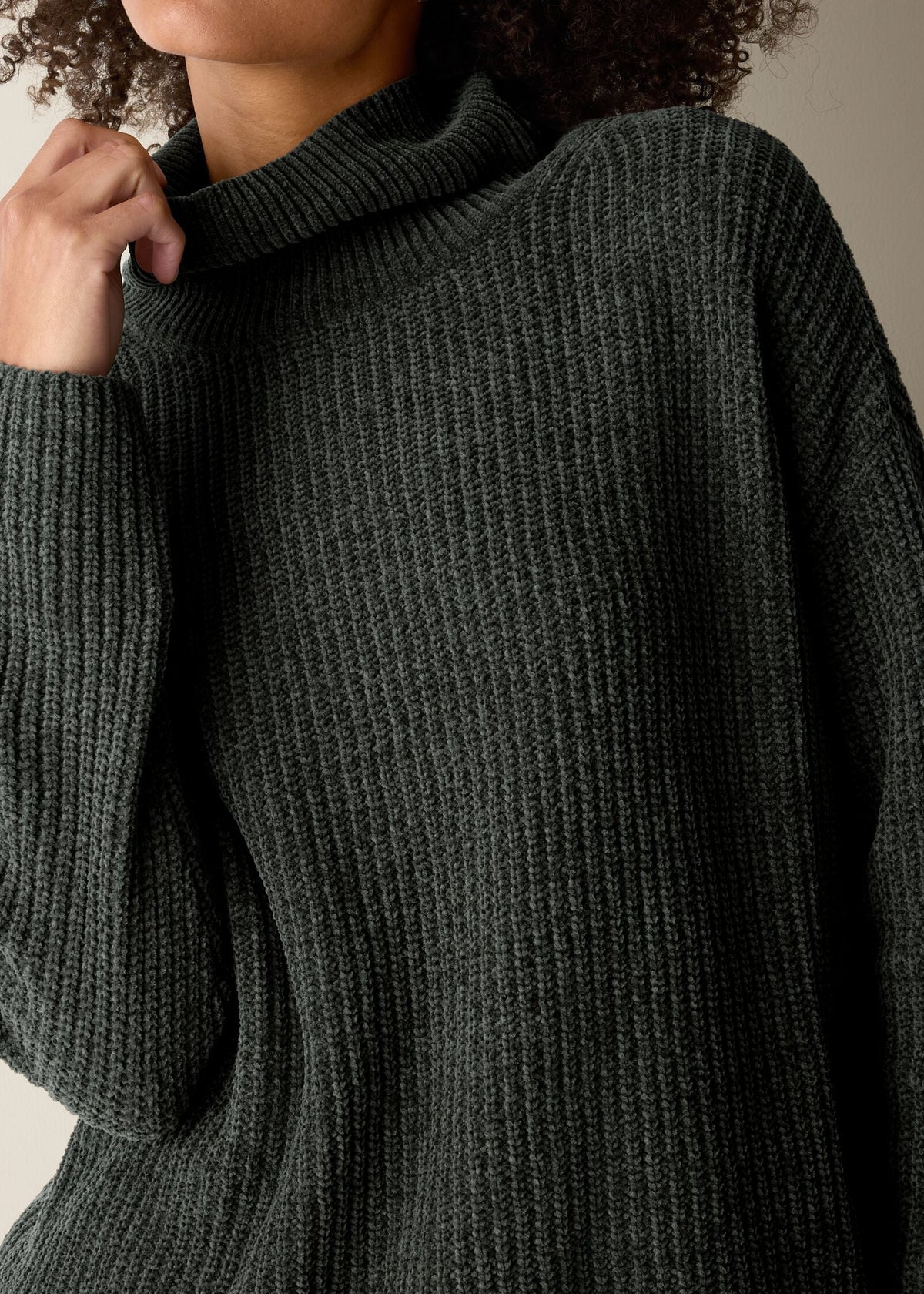 Close-up of a person wearing an oversized ribbed knit turtleneck sweater in a dark charcoal gray color.