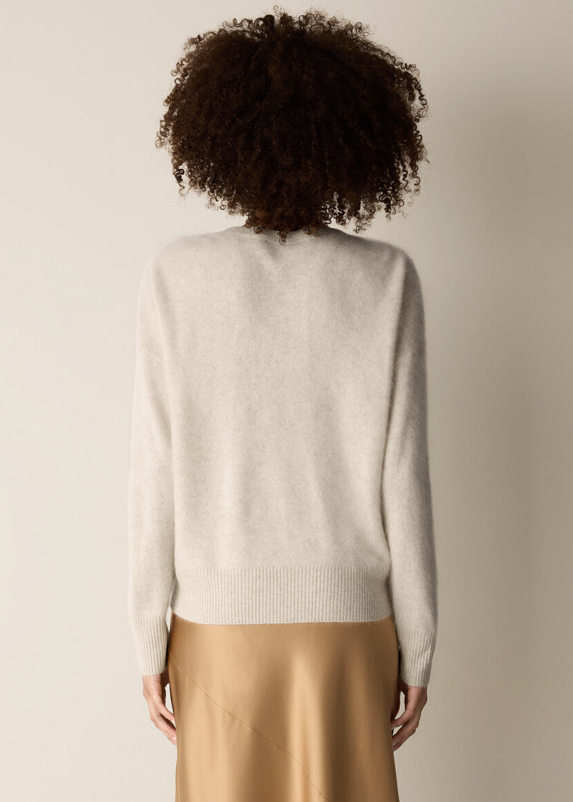 A person shown from the back wearing a light cream knit sweater and a beige satin skirt against a plain beige studio background.