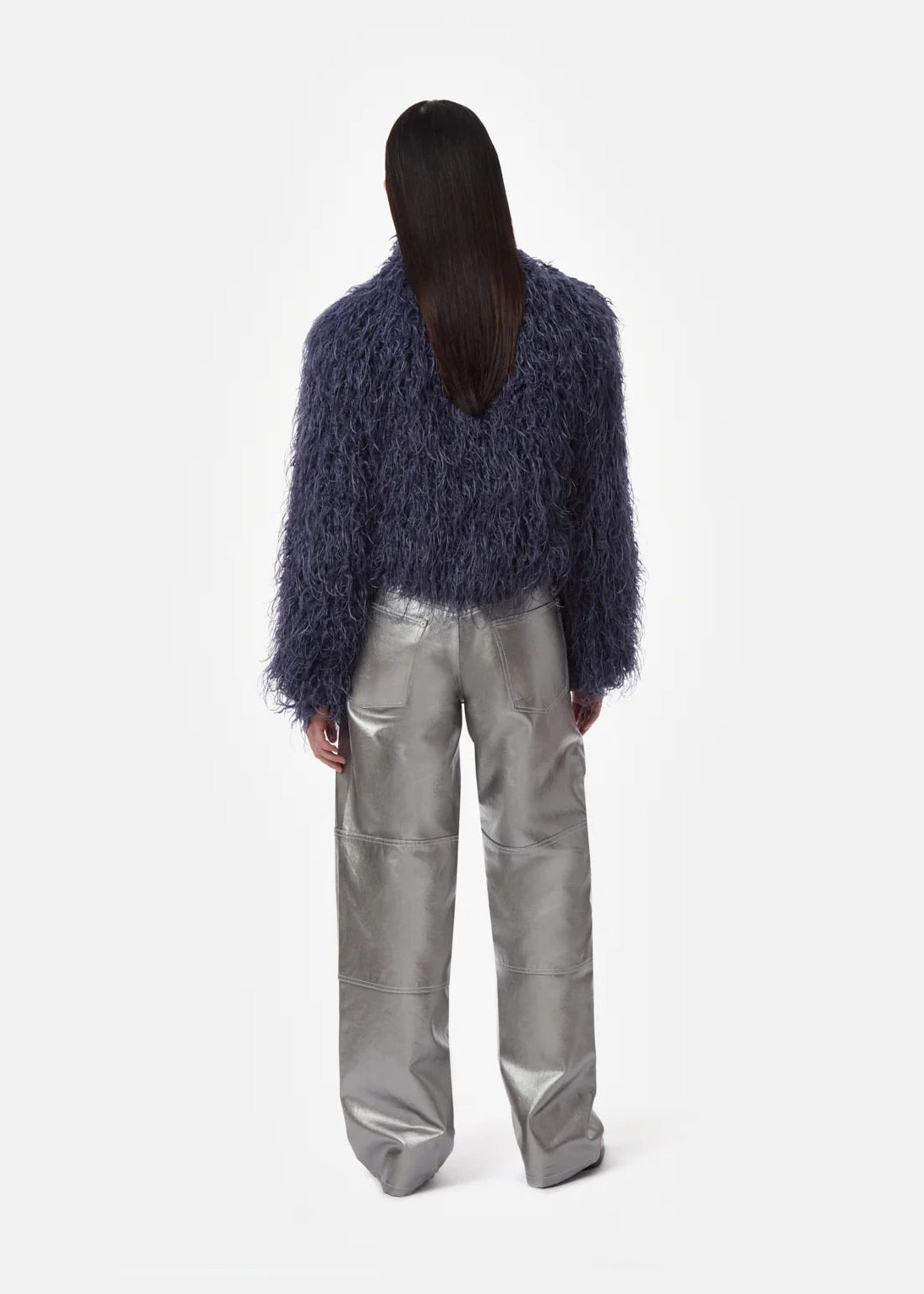 A model shown from the back wearing a dark blue shaggy cropped cardigan and shiny silver wide-leg trousers, set against a plain light gray studio background.