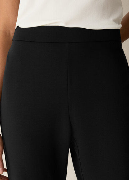 Close-up of a person wearing black wide-leg trousers with a wide elastic waistband, paired with a white top.