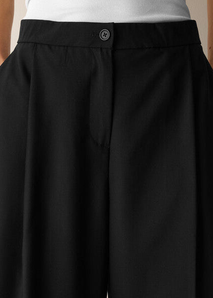 Close-up of a person wearing black wide-leg trousers with a button waistband and pleated front, paired with a white ribbed top.