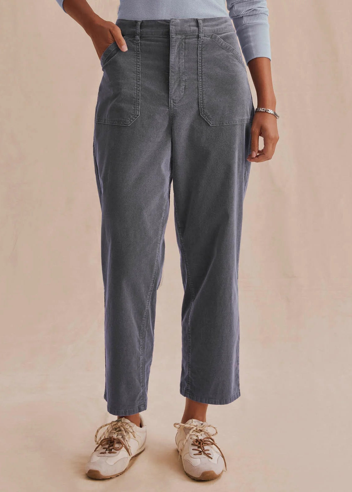 A person wearing high-waisted, wide-leg cropped pants in a faded charcoal gray color, styled with a light blue long-sleeve top and beige sneakers against a solid beige backdrop.