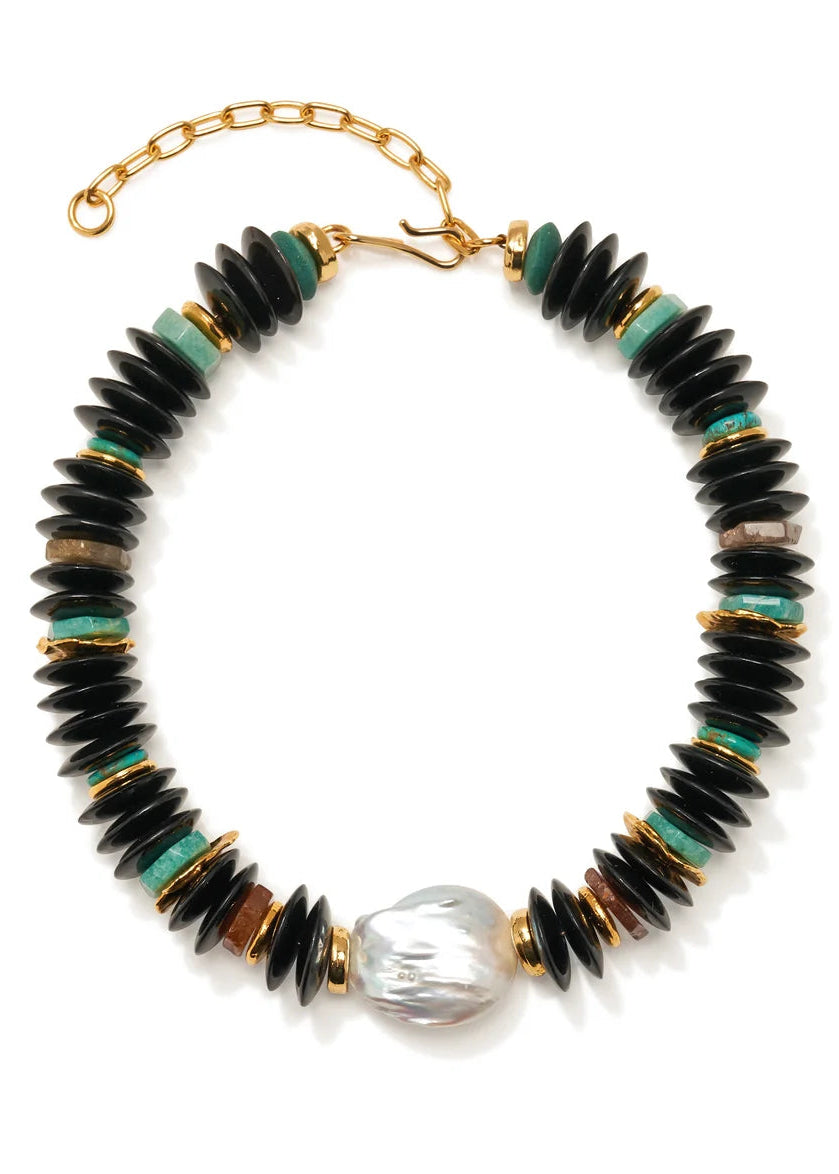 A beaded necklace featuring black disc-shaped beads, small turquoise green beads, gold spacer rings, and a large irregular white pearl at the bottom center, displayed on a clean white background.