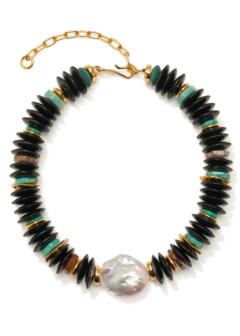 A beaded necklace featuring black disc-shaped beads, small turquoise green beads, gold spacer rings, and a large irregular white pearl at the bottom center, displayed on a clean white background.
