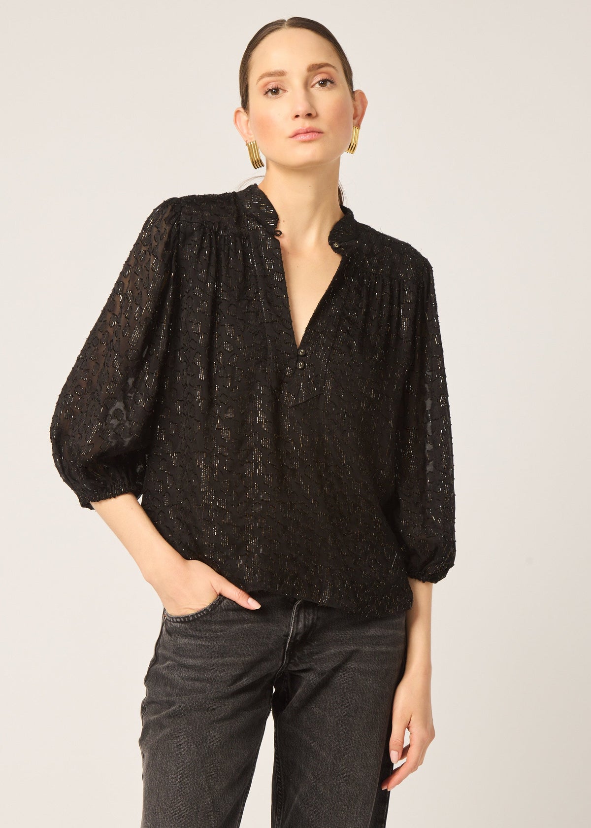 Woman wearing a black lace blouse and black pants on a light gray background