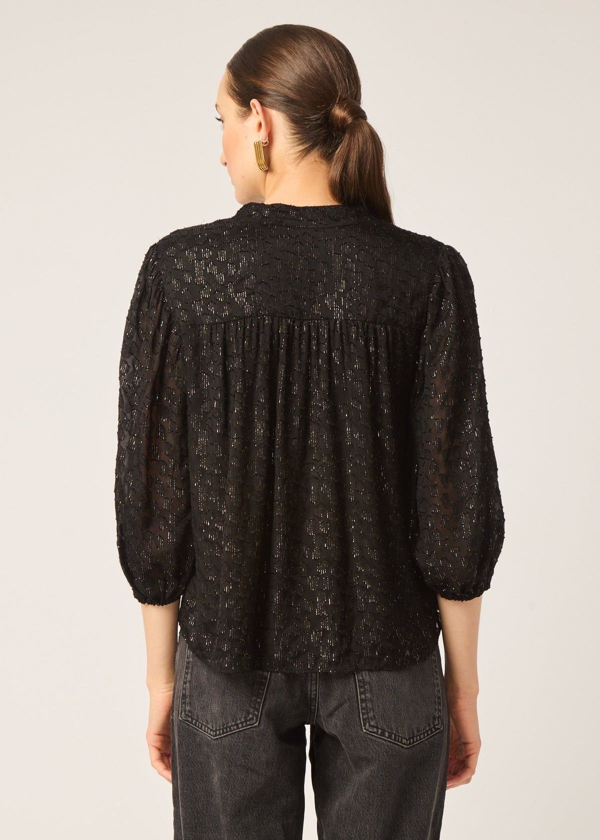 Person wearing a black lace blouse with a plain background
