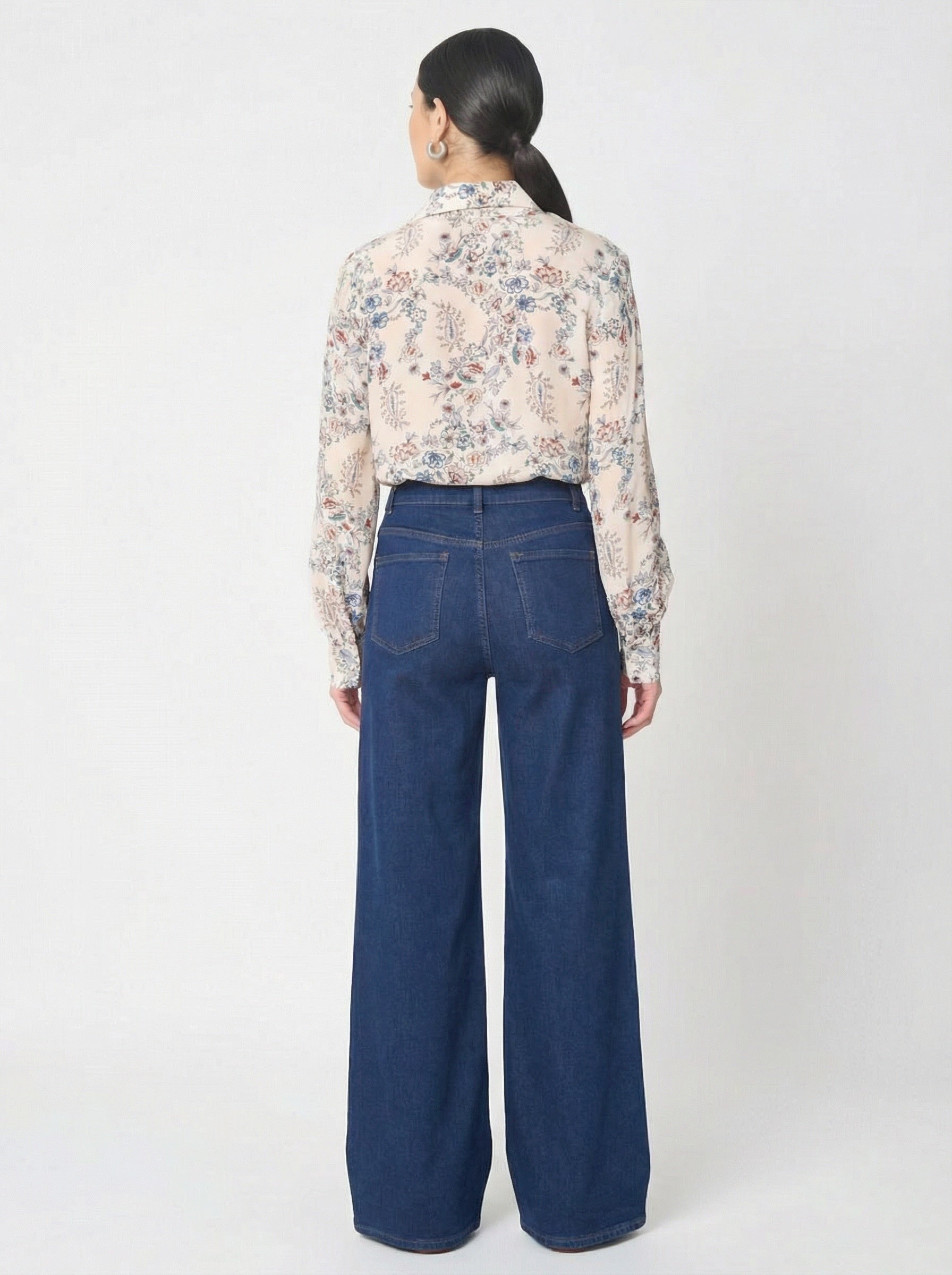 Person wearing a floral blouse and blue jeans on a white background