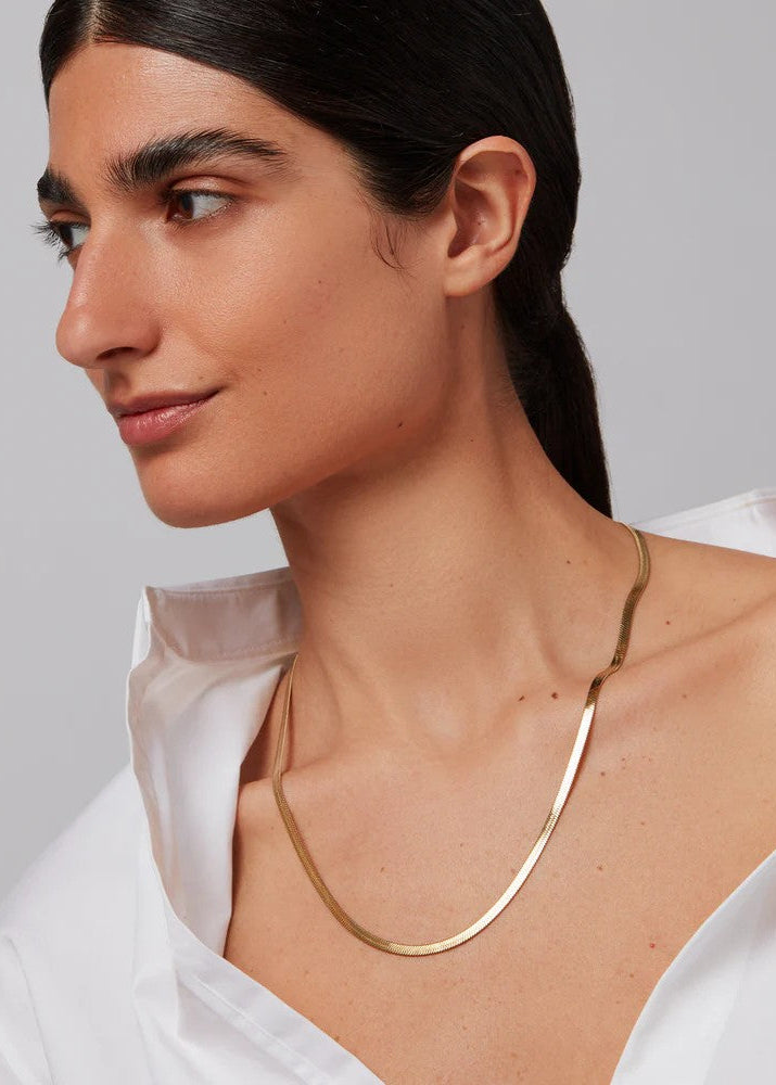 Woman wearing a gold necklace against a neutral background