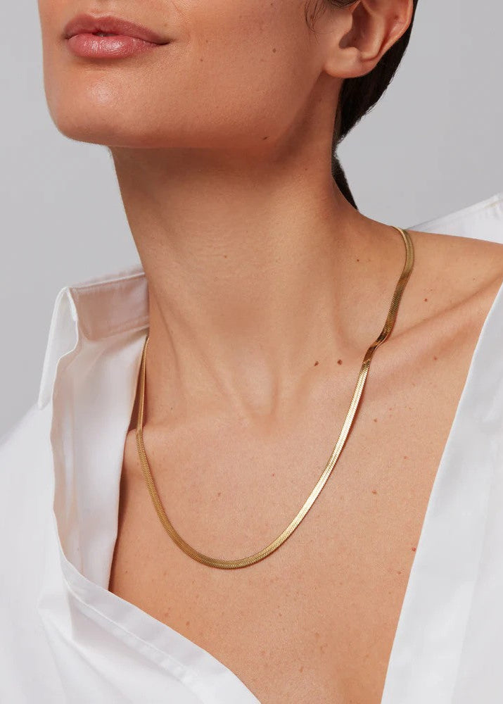 Gold necklace worn by a person against a neutral background