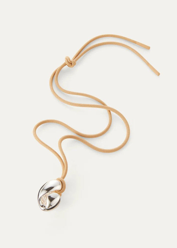 A tan suede tie-neck necklace with a polished silver-toned metallic pendant, displayed on a light cream background.