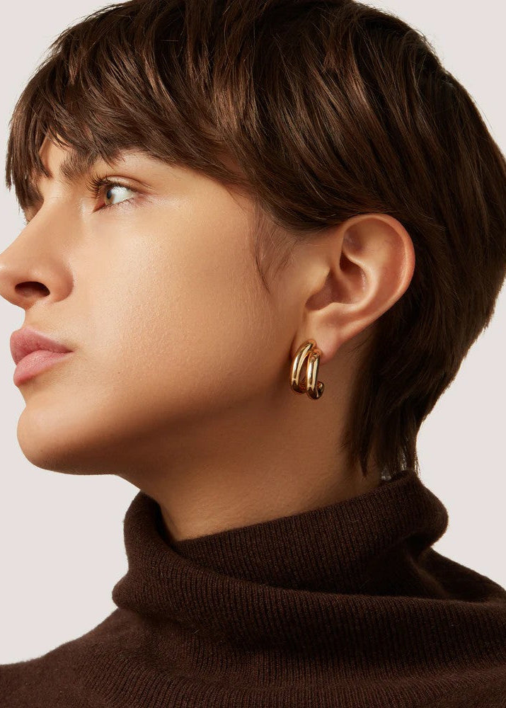 Woman wearing gold hoop earrings with a plain background