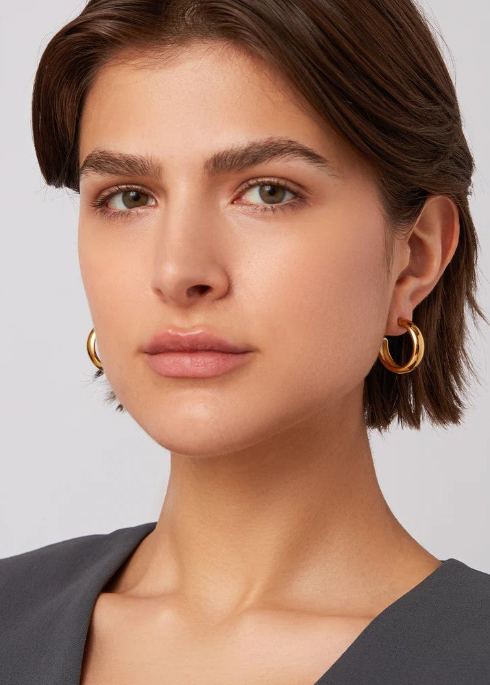 Woman wearing gold hoop earrings against a neutral background