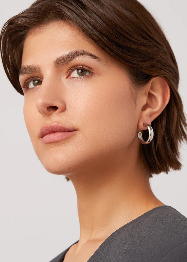 Close-up of a woman wearing a silver hoop earring against a plain background