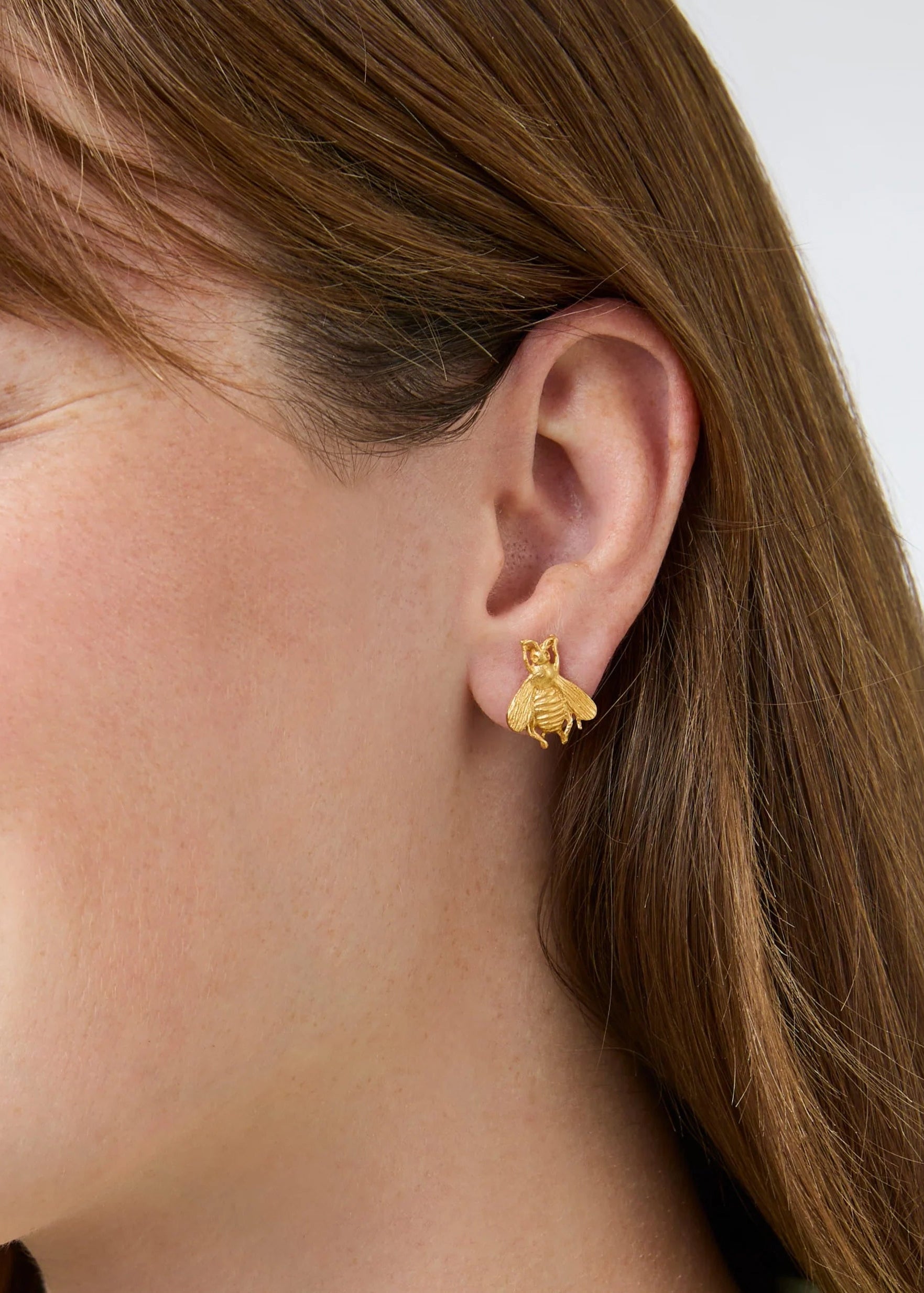 Close-up of a woman wearing gold bee earrings with a plain background