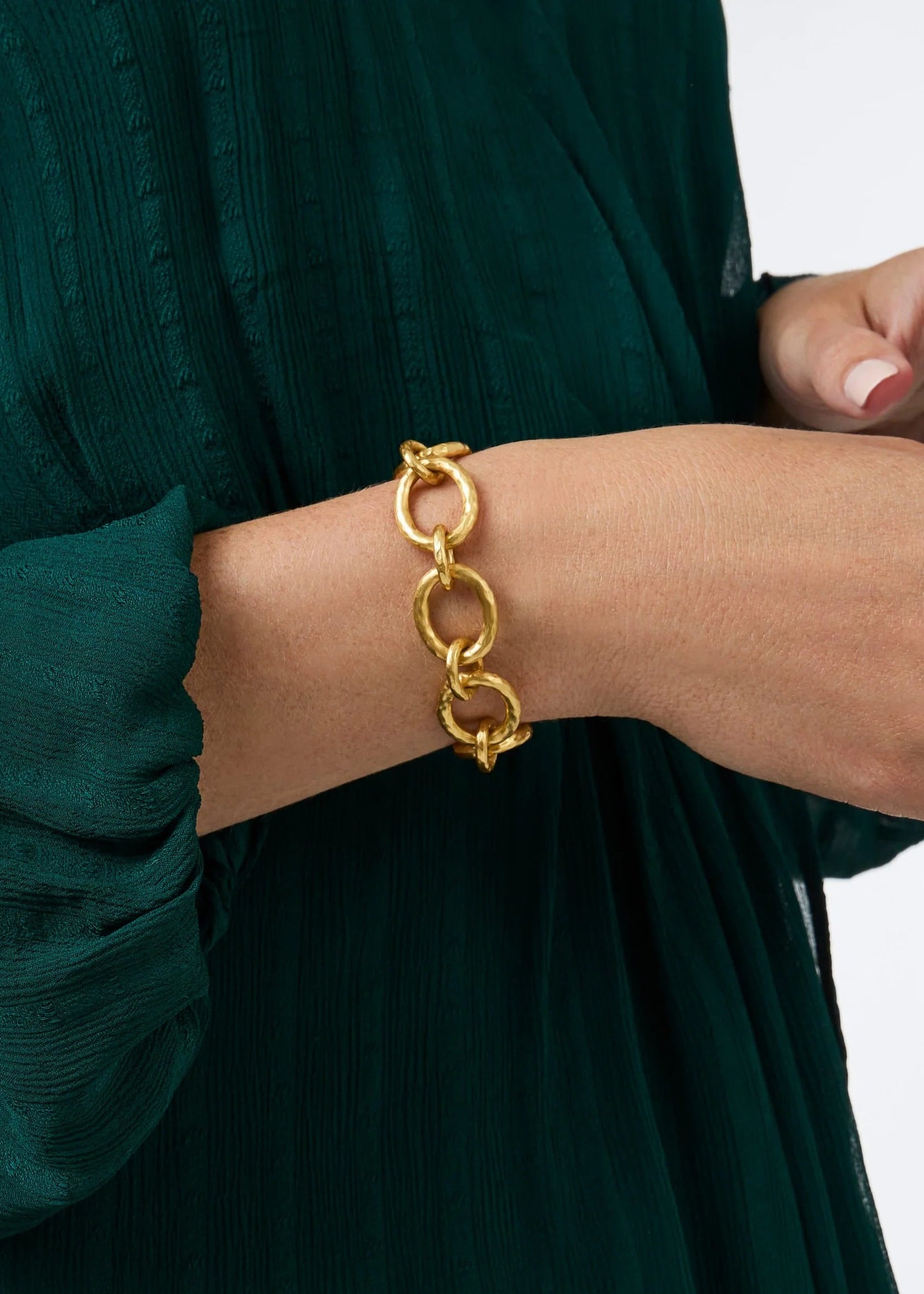 Gold chain bracelet on a person wearing a green dress against a white background
