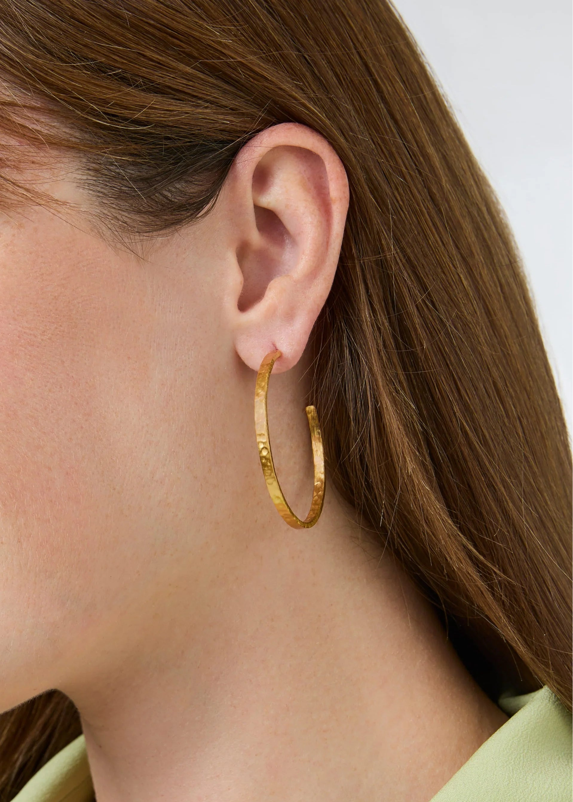 Close-up of a woman wearing gold hoop earrings with a neutral background