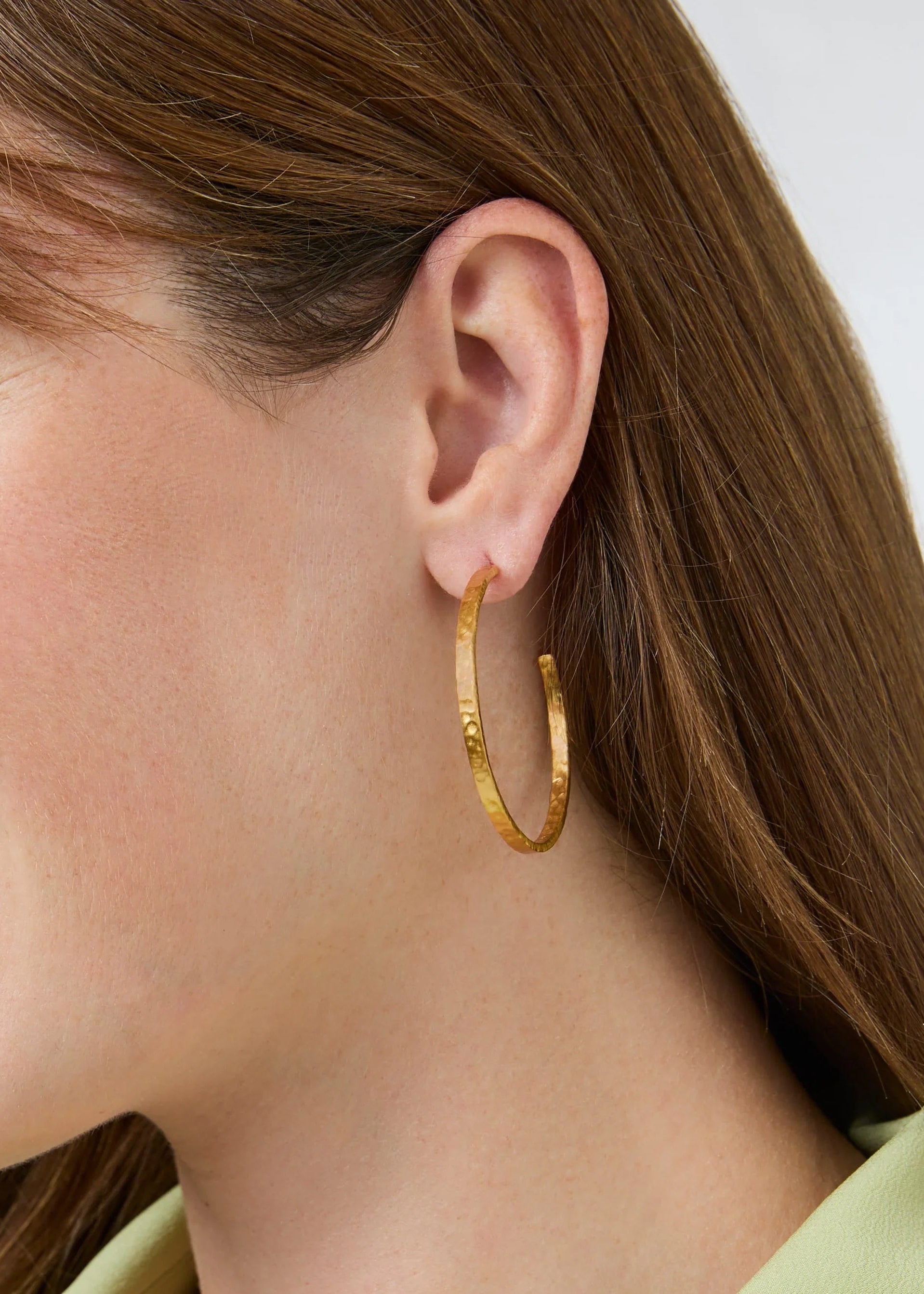 Close-up of a woman wearing gold hoop earrings with a neutral background