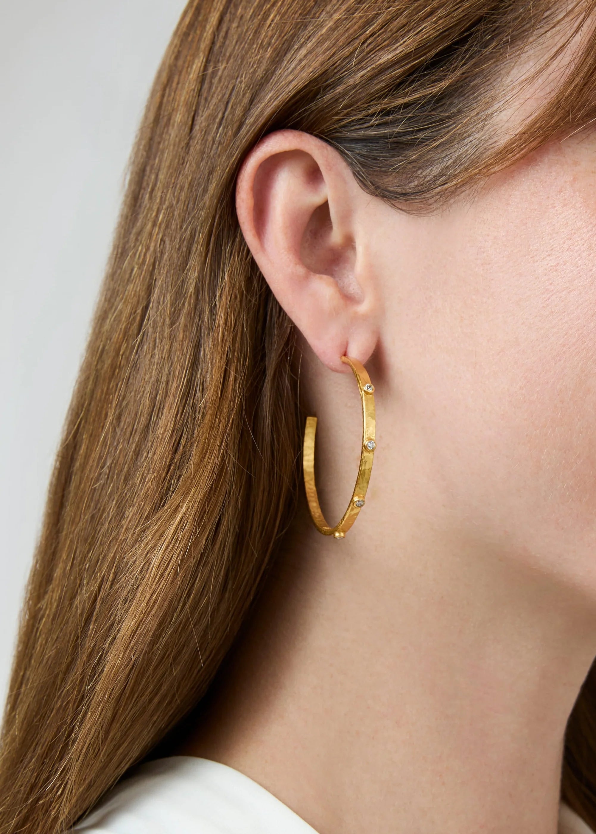 Close-up of a woman wearing gold hoop earrings with a plain background