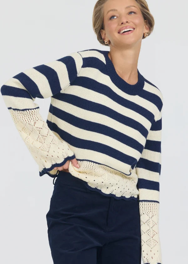 Woman wearing a navy and white striped sweater with lace details on a plain background
