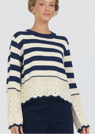 Woman wearing a navy and white striped sweater with crochet detailing on a plain background