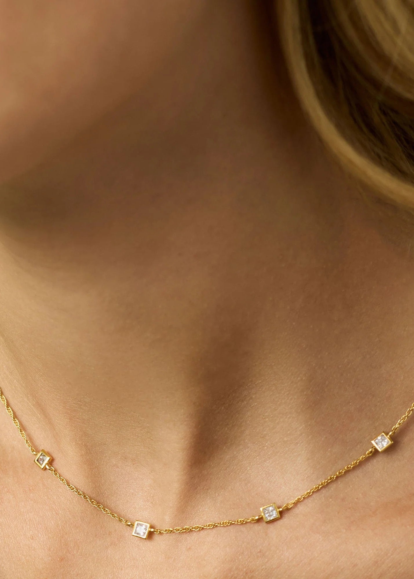 Gold necklace with small diamonds on a person wearing a green top.