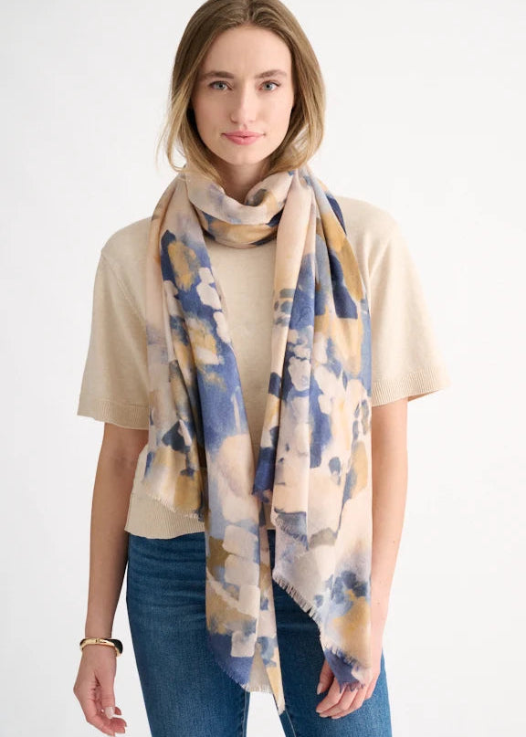 Woman wearing a beige t-shirt and blue jeans with a large, patterned scarf draped over her shoulders against a white background.