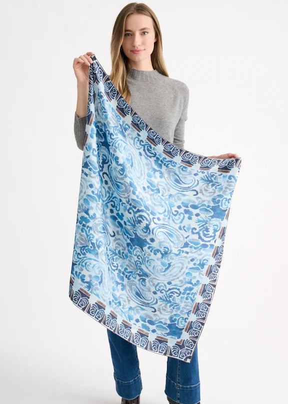 Woman holding a large blue patterned scarf against a white background