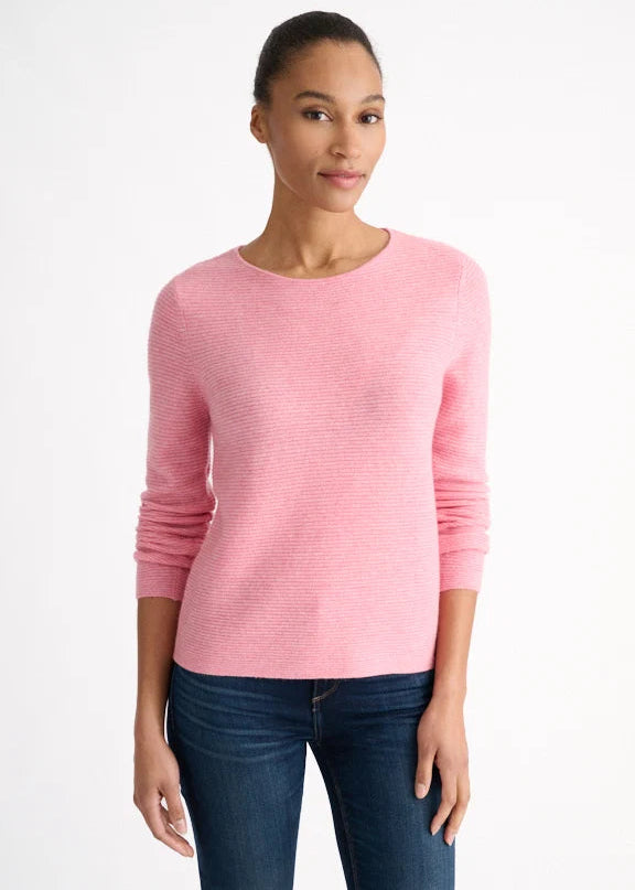 A woman modeling a light pink long-sleeve knit sweater with a crew neck, paired with dark blue jeans, against a plain white studio background.