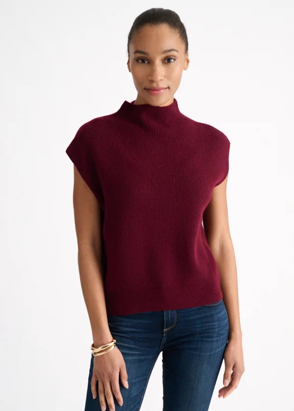 Woman wearing a burgundy sleeveless sweater and blue jeans on a white background