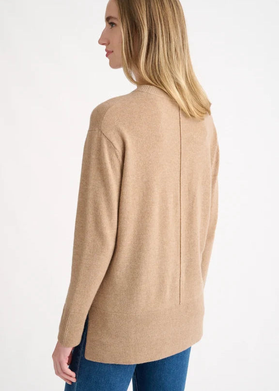 A woman shown from the back wearing a light tan knit sweater and blue jeans against a plain white studio background.