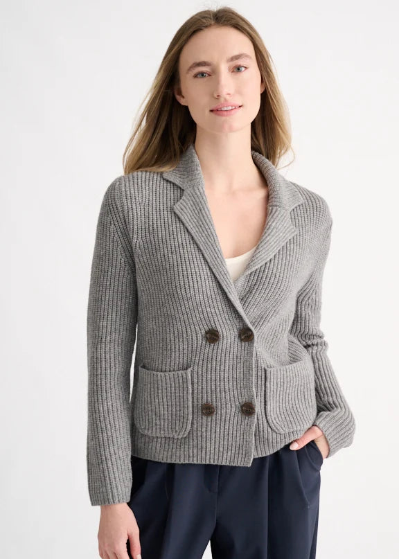 A woman modeling a light gray ribbed knit double-breasted blazer with dark brown buttons, worn over a white top and navy trousers, against a plain white studio background.