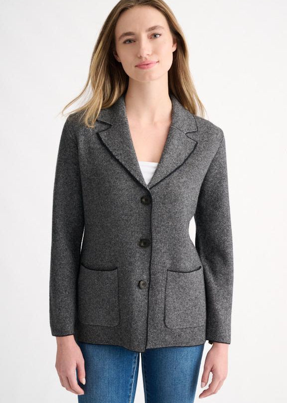 A woman modeling a dark gray textured wool blazer with black buttons and front patch pockets, paired with blue jeans, against a plain white studio background.