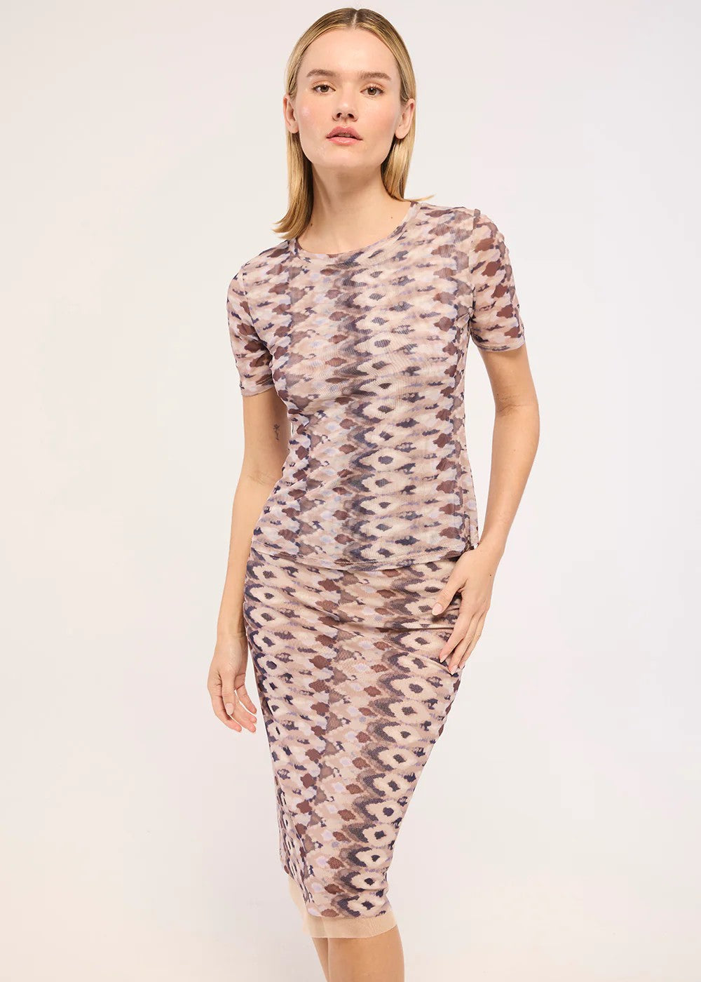 A woman modeling a short-sleeve midi dress with a beige, brown, and gray geometric pattern against a plain light background.