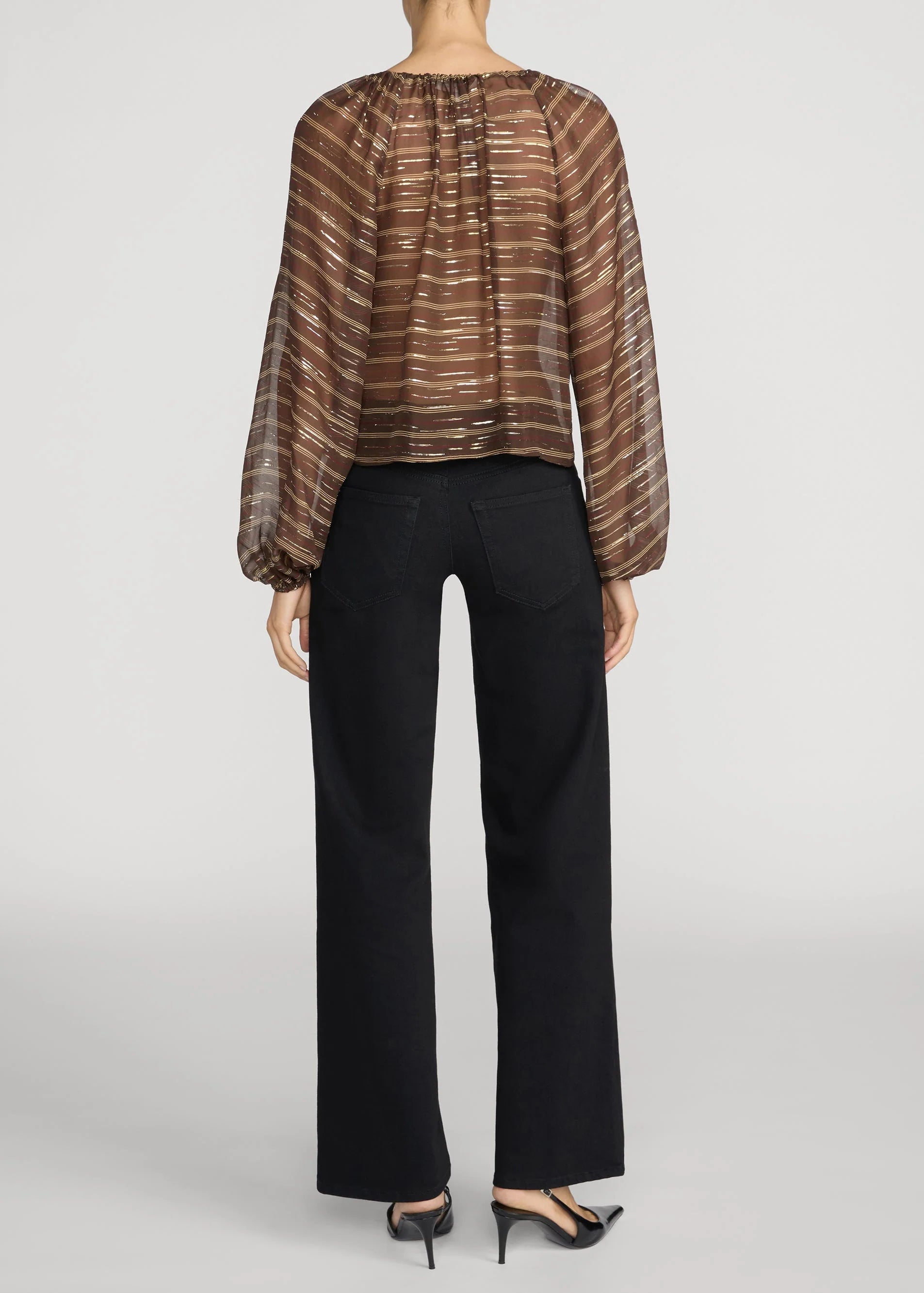 A model shown from the back wearing a brown sheer striped long-sleeve blouse and black wide-leg trousers, paired with black heels, against a light gray studio background.