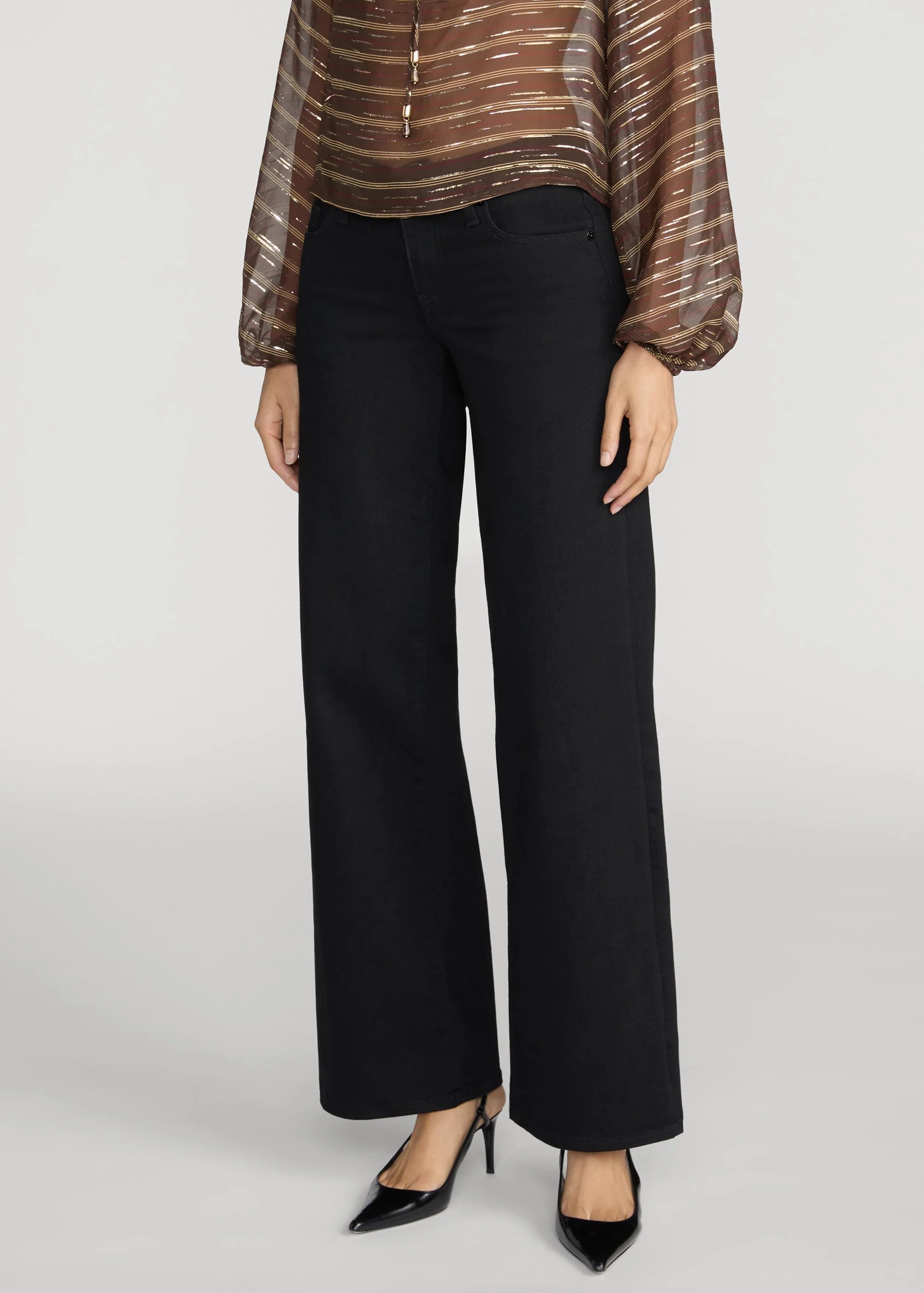 A model is shown from the waist down wearing black wide-leg trousers, a brown and gold striped sheer blouse, and black pointed-toe heels against a light gray studio background.