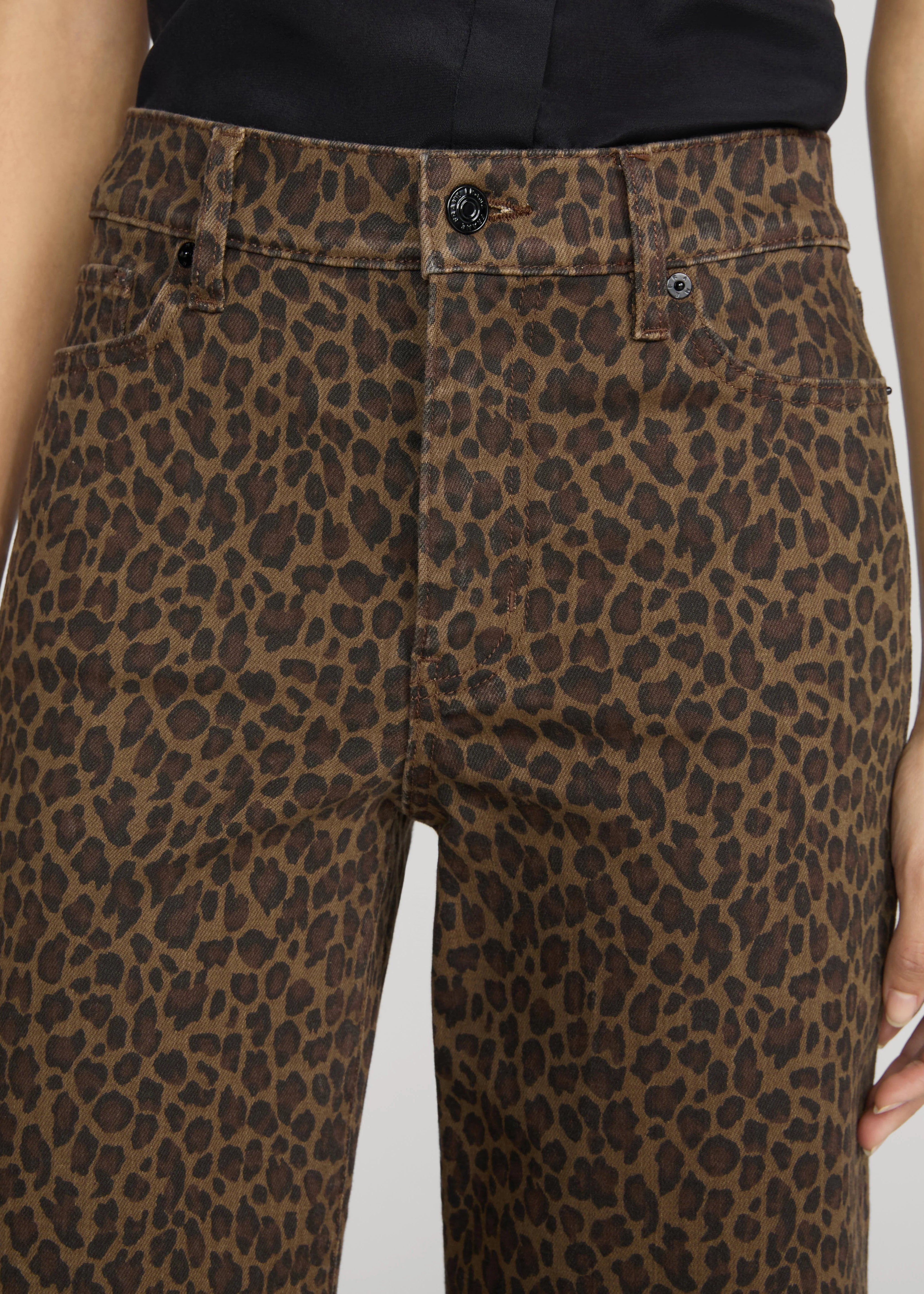 Close-up of a person wearing leopard-print jeans with a brown and black animal pattern, paired with a dark top against a light gray background.
