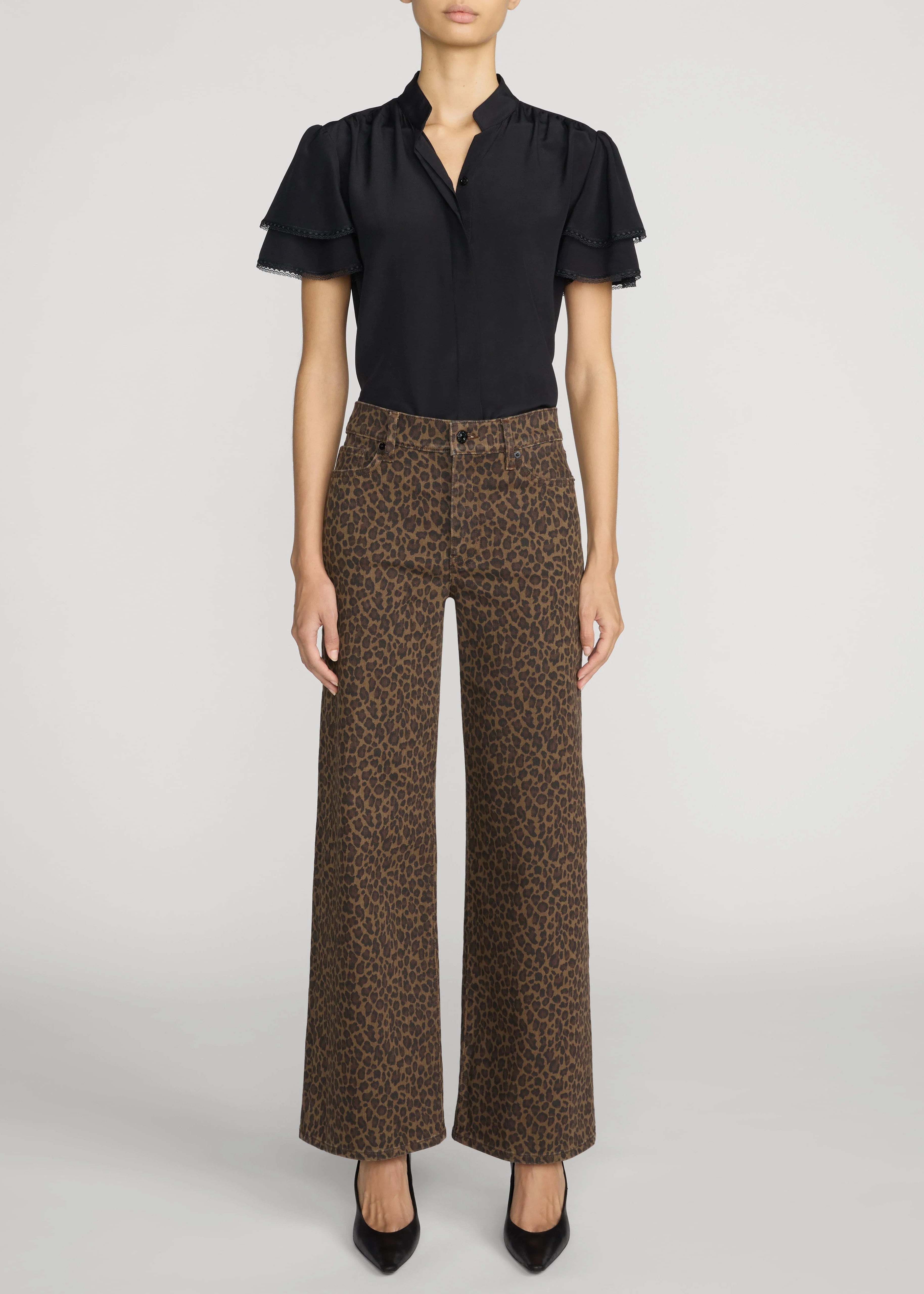A model wearing a black short-sleeve blouse with ruffled sleeves and brown leopard-print wide-leg trousers, paired with black pointed-toe heels, against a light gray studio background.