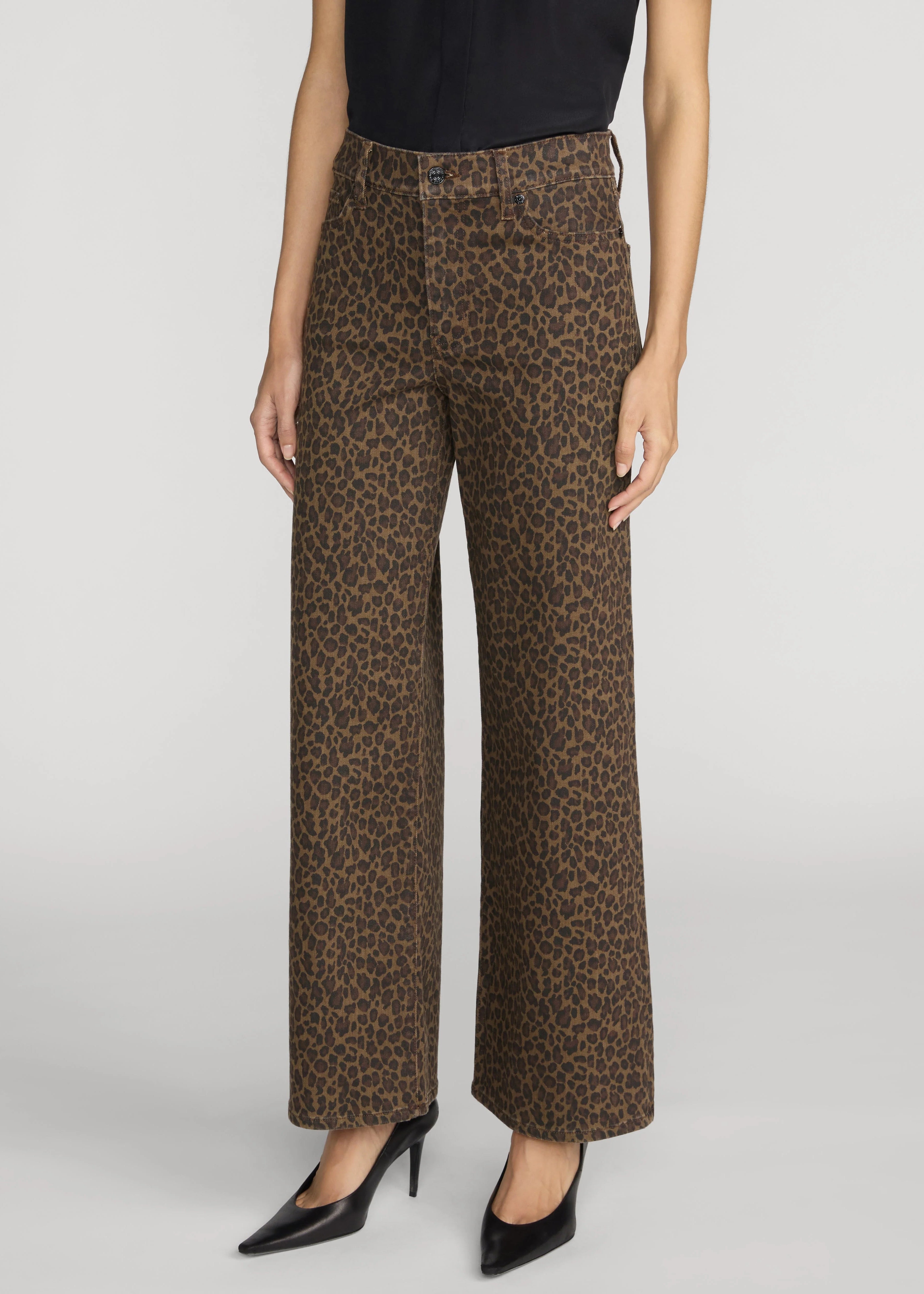 A model wearing brown leopard-print wide-leg pants with a black top and black pointed-toe heels, shown from the waist down on a light gray studio background.