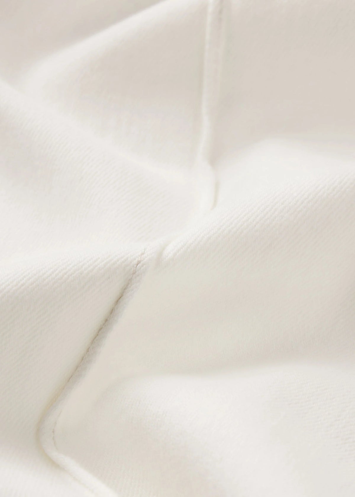 A close-up of a soft off-white fabric with visible texture and a curved seam.