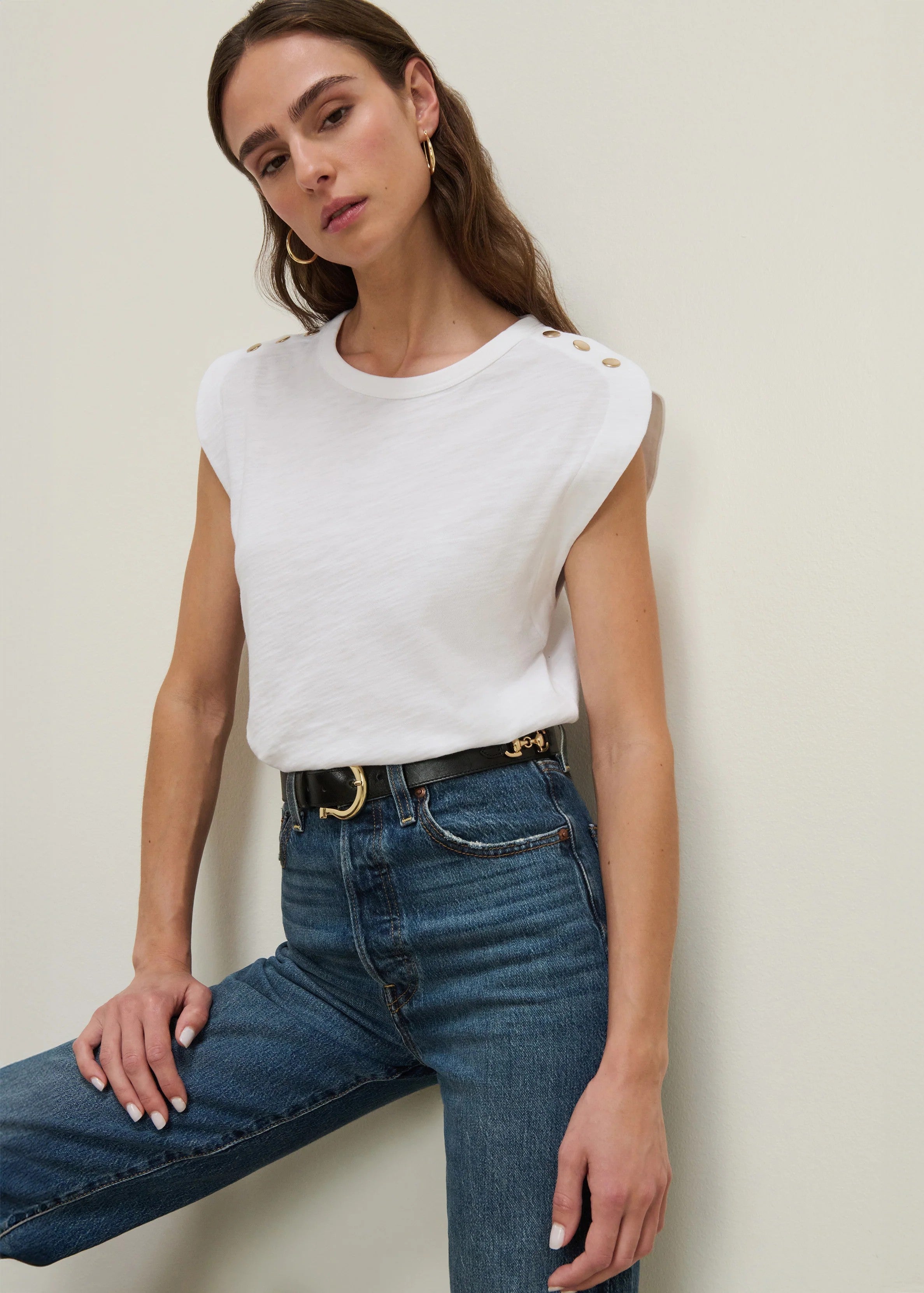 Woman wearing a white sleeveless top and blue jeans against a plain background